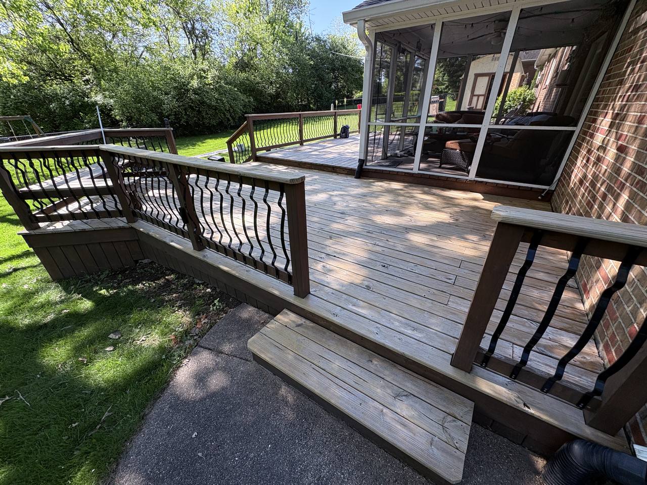 Weathered grey wood deck and railing beside a brick house, seen from the walkway